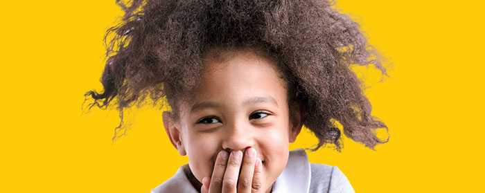 A child smilling as she covers her mouth