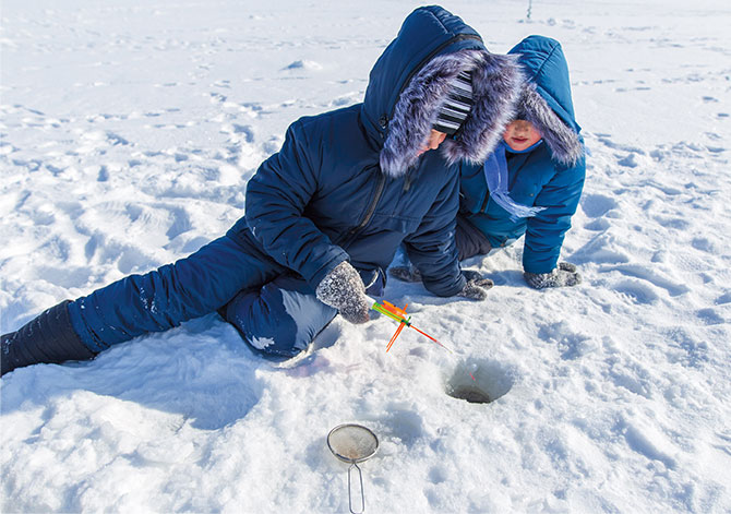 Enlargeable photo of two kids dressed in heavy winter coats fishing through a hole in the ice