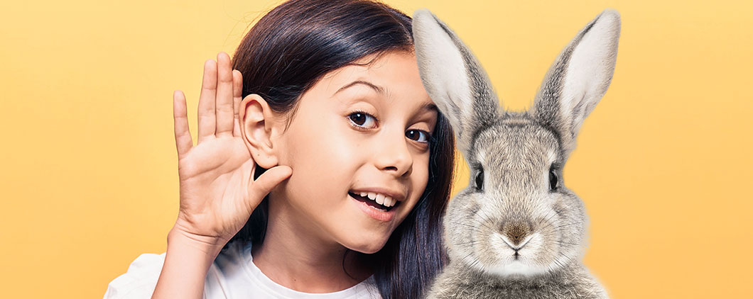 a girl holding her hands up next to her ear and sitting next to a rabbit