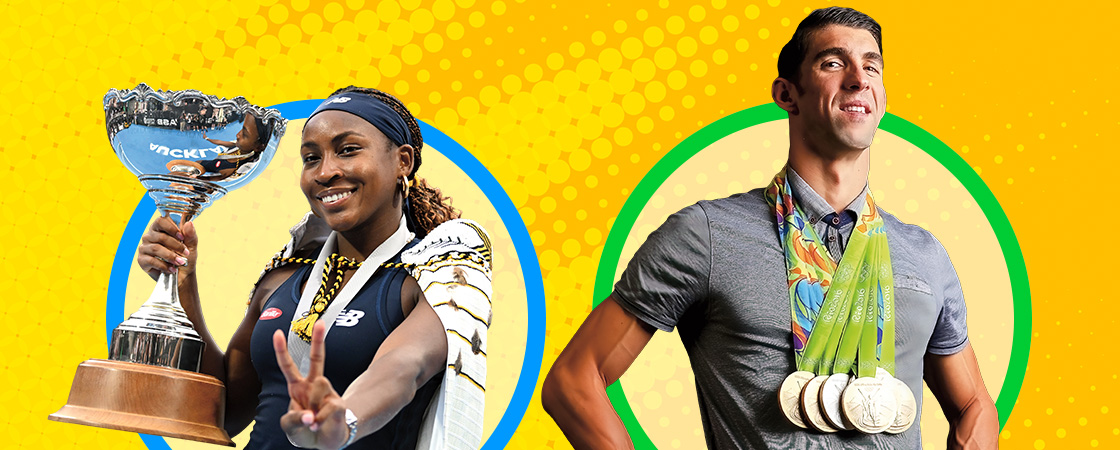 Image of two Olympians posing with large trophy and gold medals