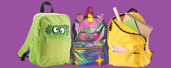 Three colorful children's backpacks: a green monster, a unicorn, and a yellow pack filled with school supplies